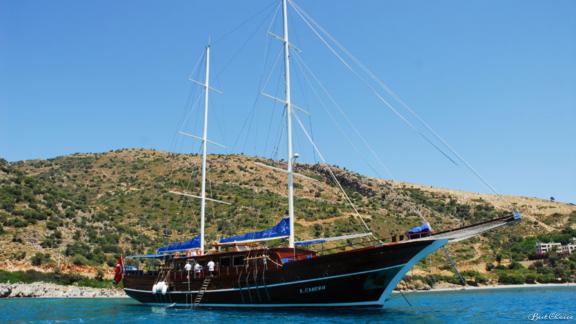 Die Gulet A Candan segelt auf klarem, blauem Wasser vor einer hügeligen Küste.